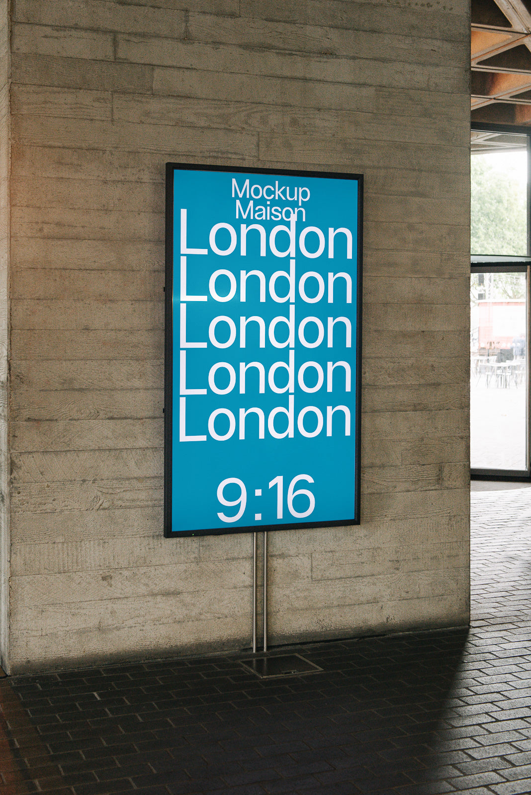 PSD mockup of a vertical digital signage display showcasing repeated text "London" on a blue background, mounted on a concrete wall indoors.