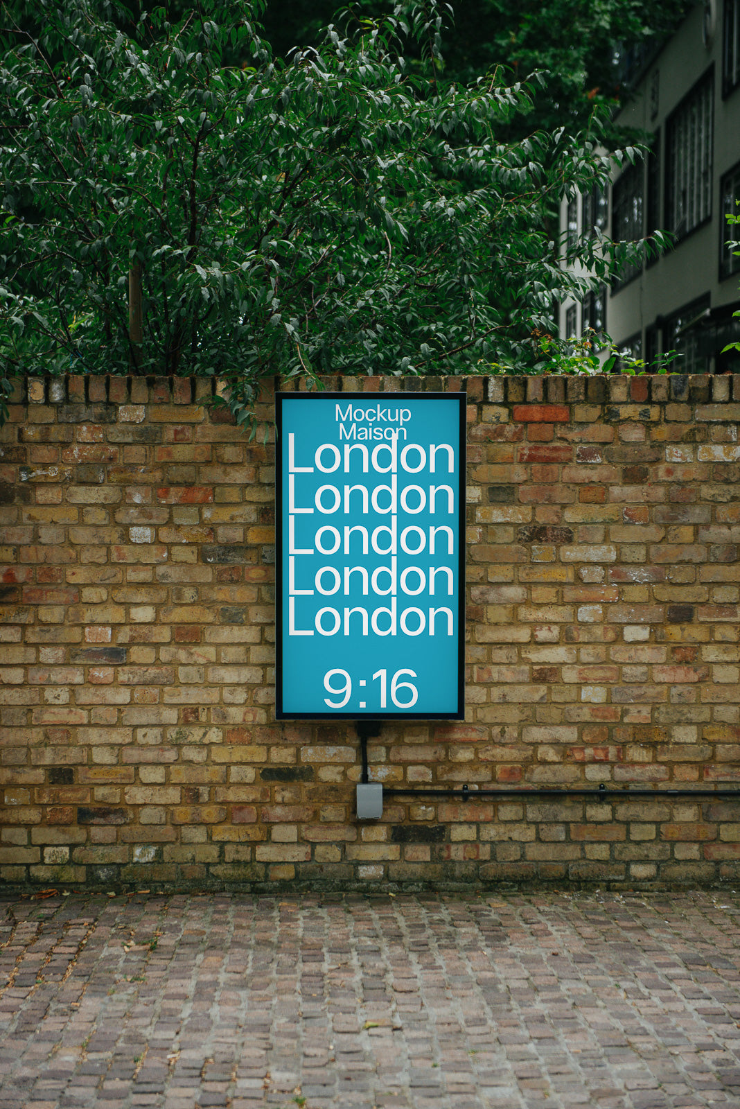 PSD mockup of a vertical signage on a brick wall displaying the word "London" in bold text with a digital clock reading 9:16 against a leafy background.