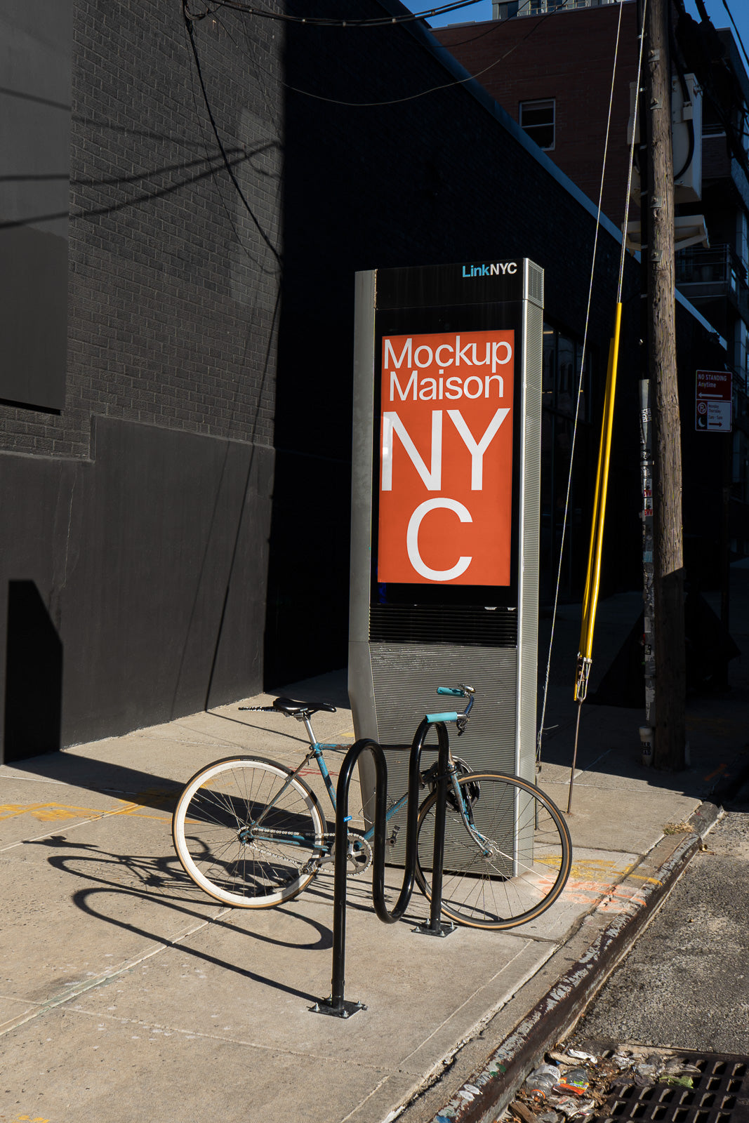 PSD mockup of a LinkNYC kiosk with vibrant orange signage displaying "Mockup Maison NYC", accompanied by a parked blue bicycle on a sunny city sidewalk.