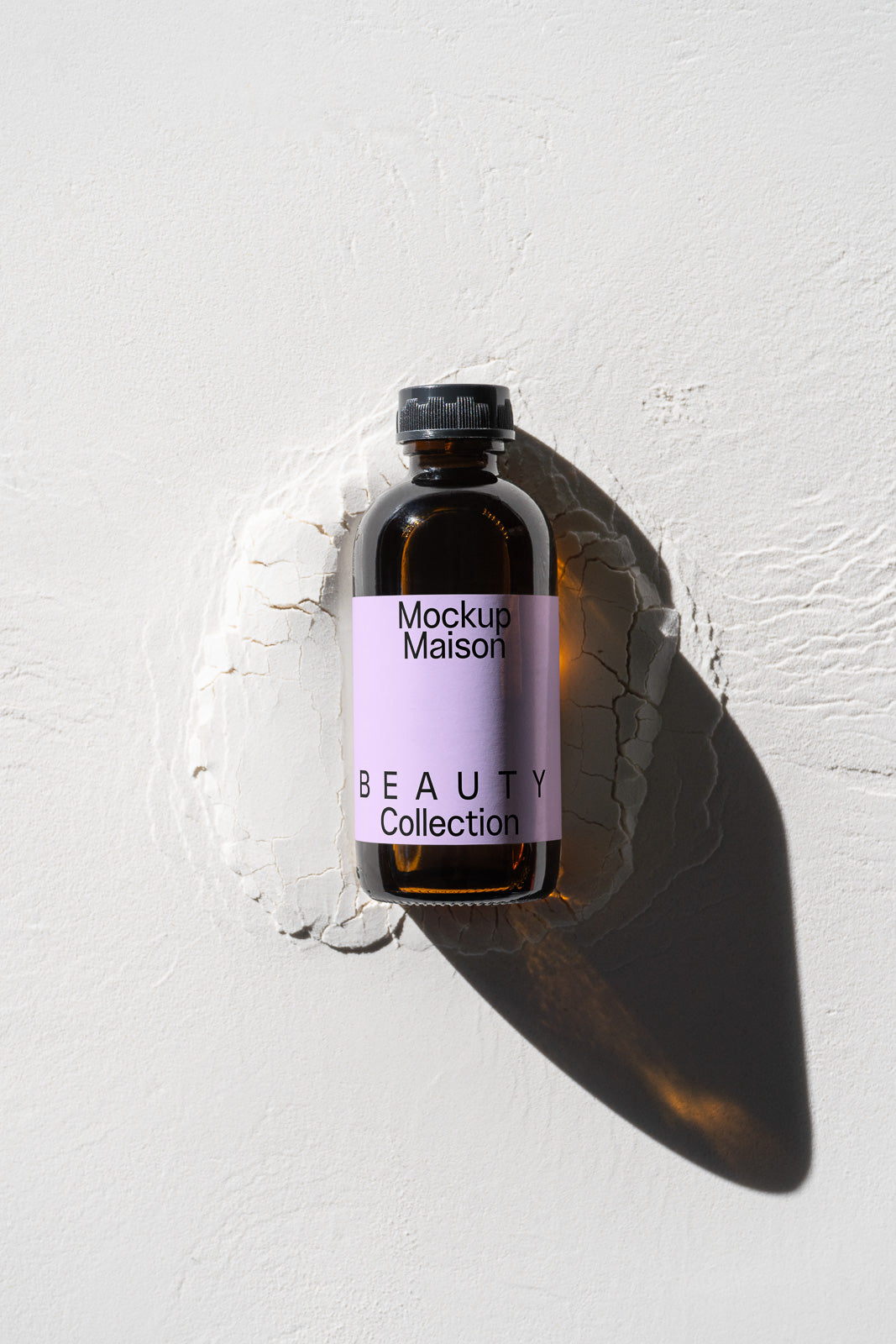 PSD mockup of an amber glass bottle with a black cap, featuring a purple label marked "Mockup Maison" and "BEAUTY Collection" against a textured surface.