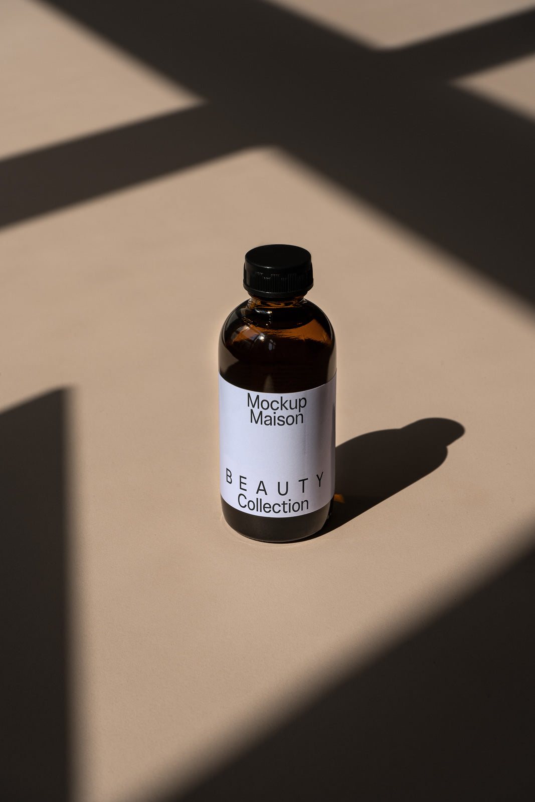 PSD mockup of a brown glass bottle with white label in a sunlit scene, labeled "Mockup Maison Beauty Collection" on a neutral background.