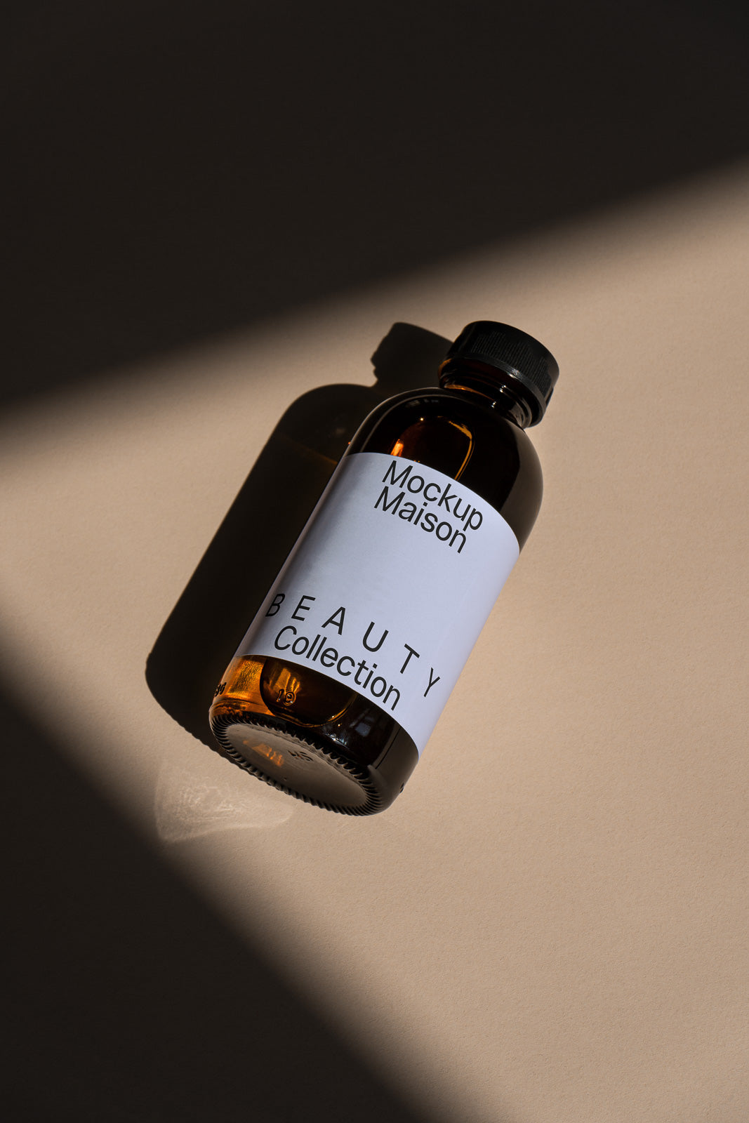 PSD mockup of an amber glass bottle with "Mockup Maison Beauty Collection" label, casting a shadow on a beige surface.