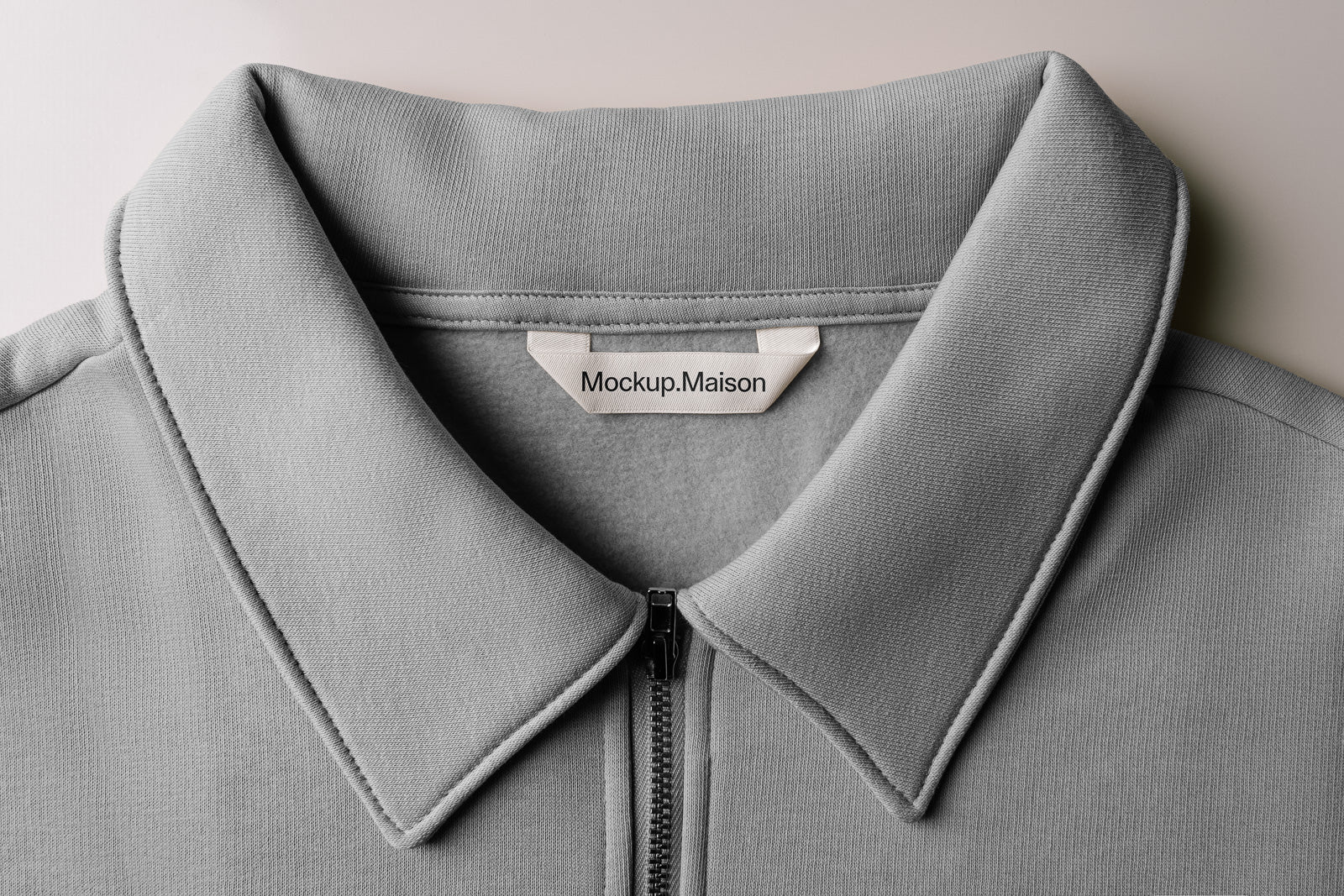 PSD mockup of a gray zipped polo shirt with a wide collar, showcasing detailed fabric texture and a sewn-in tag labeled "Mockup.Maison" inside the collar.