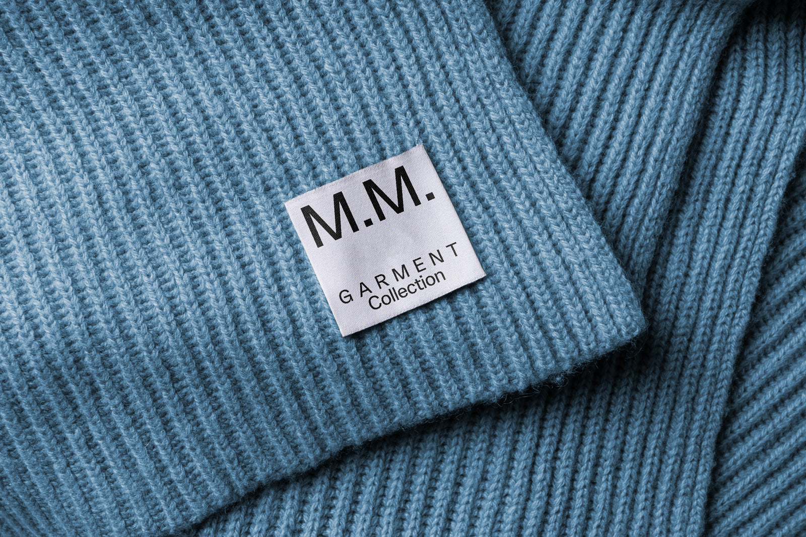 PSD mockup of a clothing label featuring the text "M.M. Garment Collection" on a textured blue fabric background.