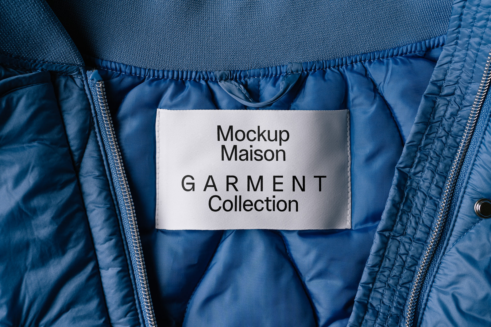 PSD mockup of a garment label inside a blue quilted jacket, displaying the text "Mockup Maison Garment Collection" on a white tag.