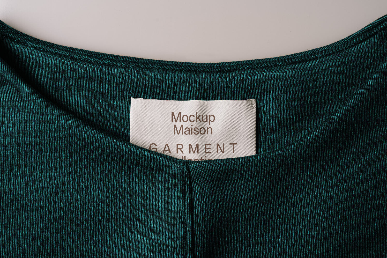 PSD mockup of a clothing label on a dark green fabric, featuring the text "Mockup Maison" and "Garment."
