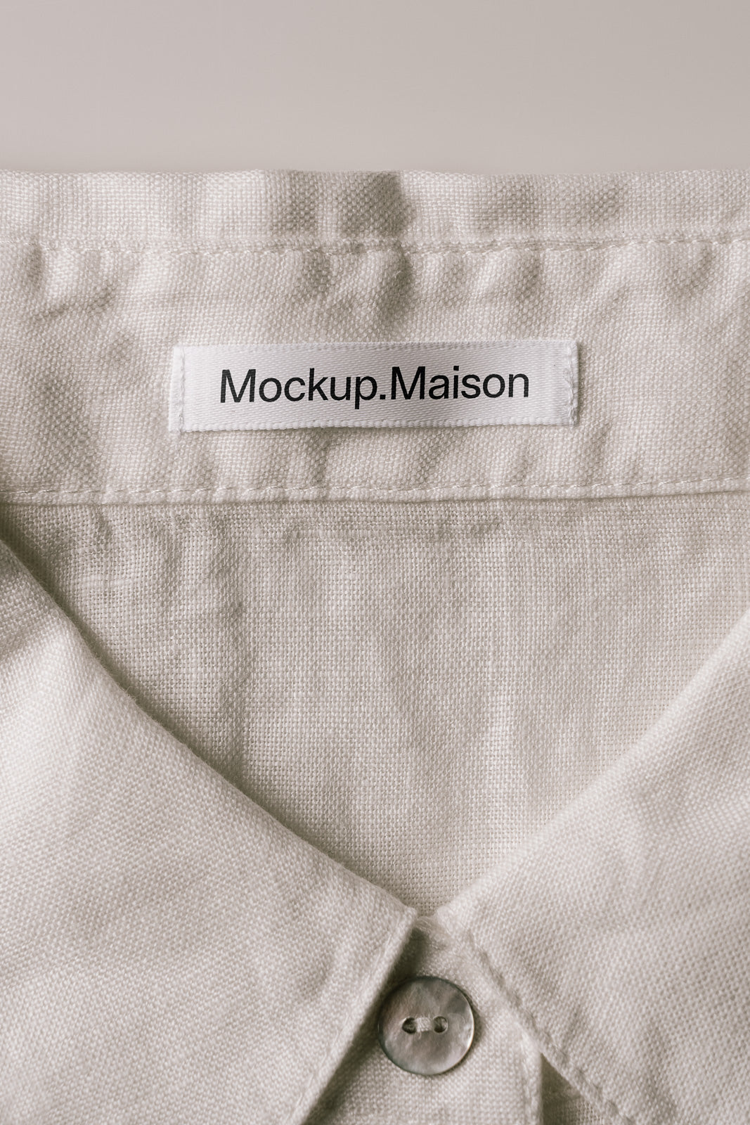 PSD mockup of a light-colored shirt collar featuring a fabric label with the text "Mockup.Maison" stitched at the back, highlighting texture and details.