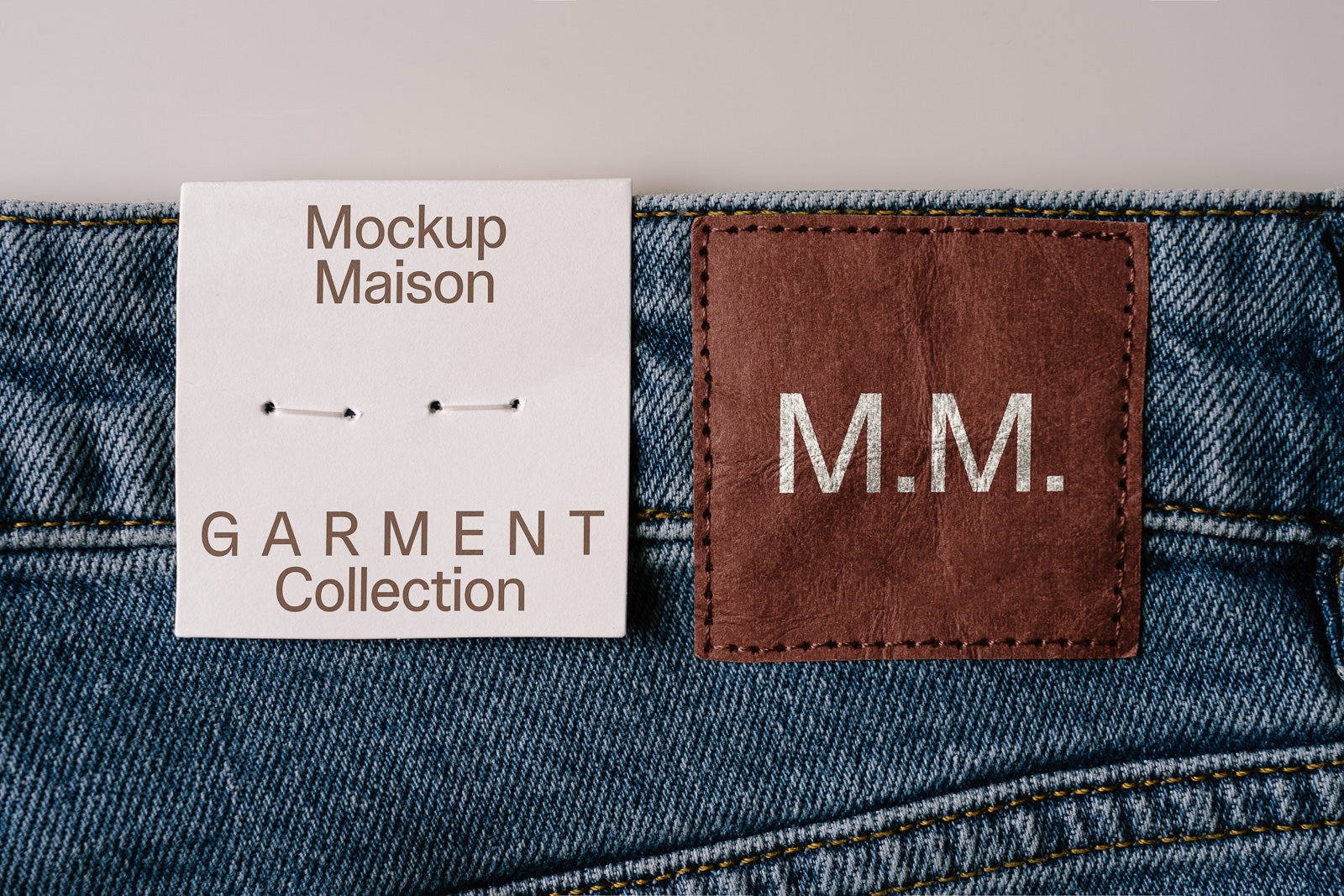 PSD mockup of a garment tag and leather patch on blue denim fabric, featuring text "Mockup Maison" and "M.M." for branding purposes.