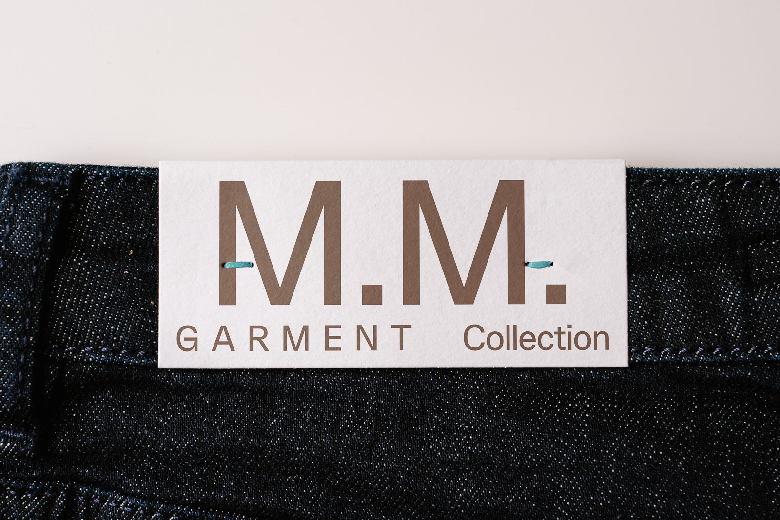 PSD mockup of a clothing label with "M.M. Garment Collection" attached to denim fabric, highlighting branding elements.
