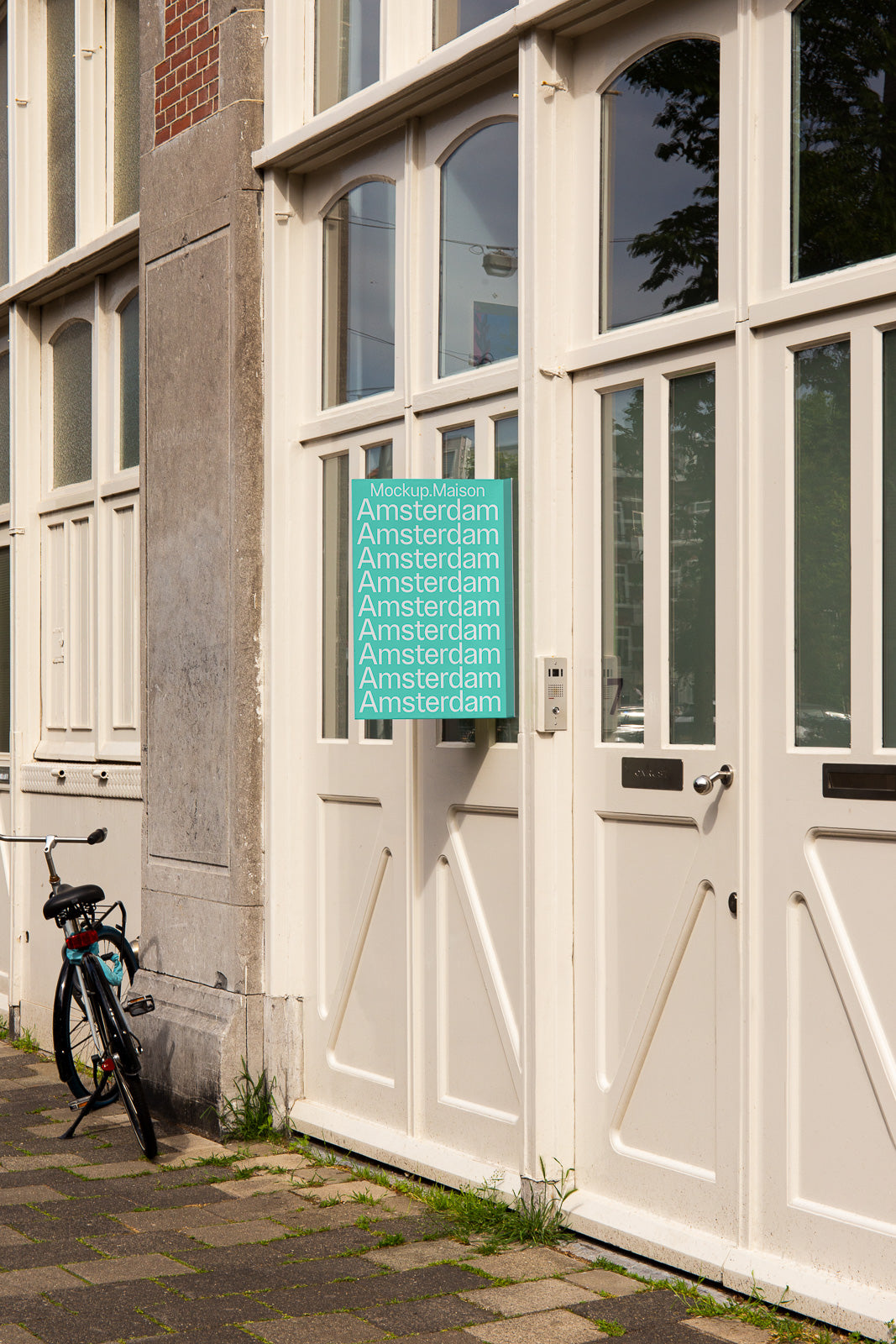 PSD mockup of a building entrance with a mint green sign displaying the word "Amsterdam" repeated multiple times. A bicycle is parked nearby.