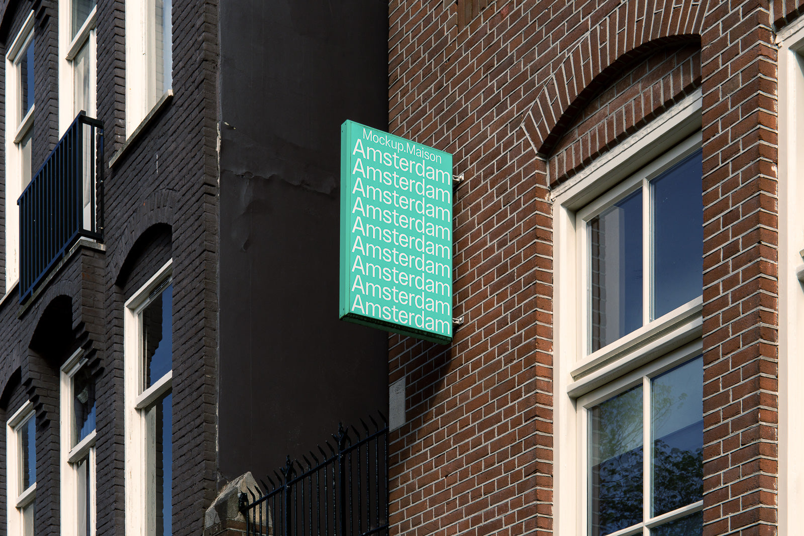 PSD mockup of a building sign with the word "Amsterdam" repeated in white on a teal background, mounted on a brick facade near windows.