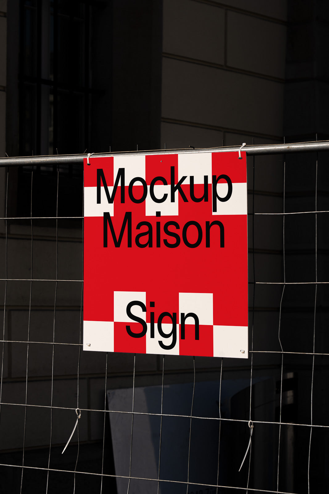 PSD mockup of a red and white checkered sign with the words "Mockup Maison Sign" hanging on a wire fence in an urban setting.