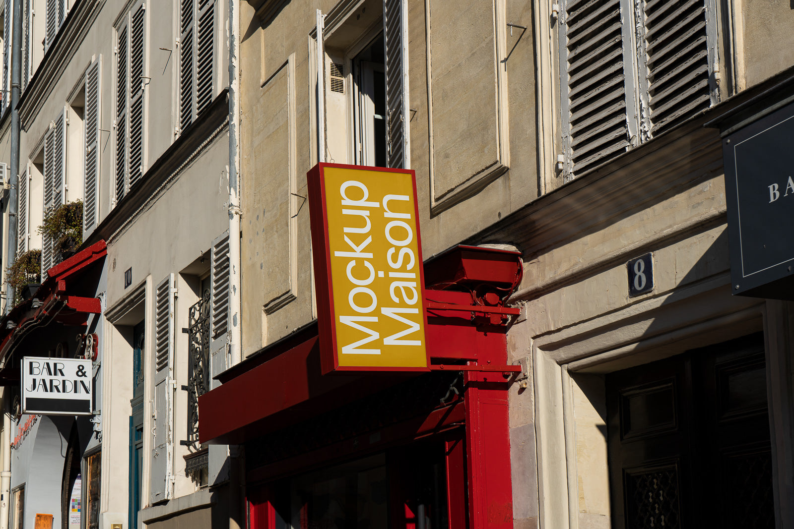 PSD mockup of an urban building facade featuring a yellow and red vertical sign reading “Mockup Maison” against a backdrop of beige walls and windows.