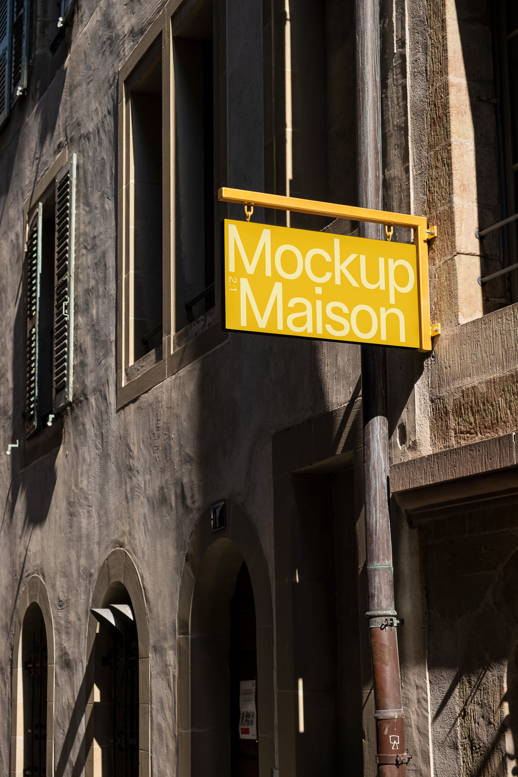 PSD mockup of a yellow rectangular signboard reading "Mockup Maison" attached to the exterior of a stone building with arched windows.