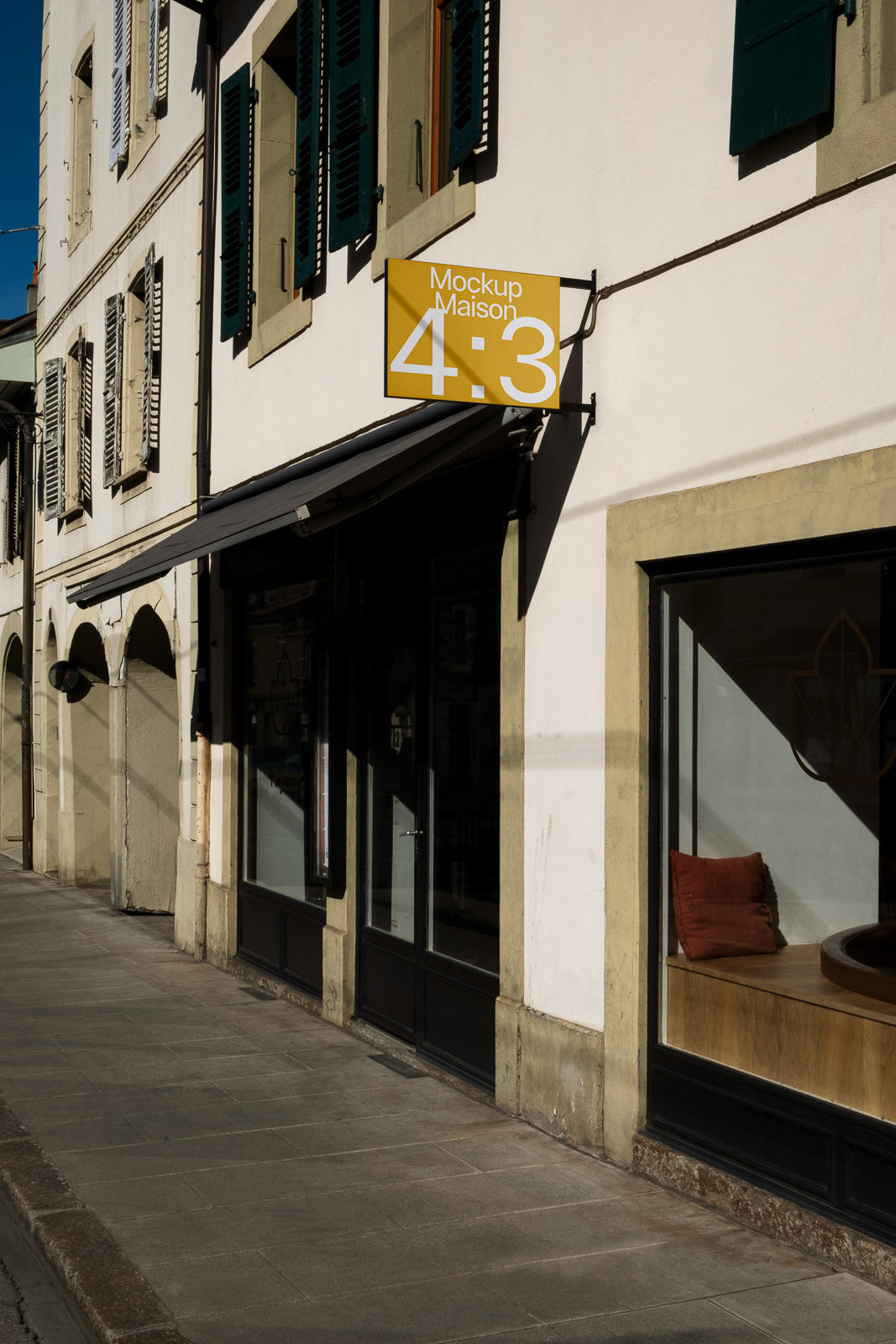 PSD mockup of a building facade with a yellow sign displaying "Mockup Maison 4:3" hanging near a window with an orange cushion.