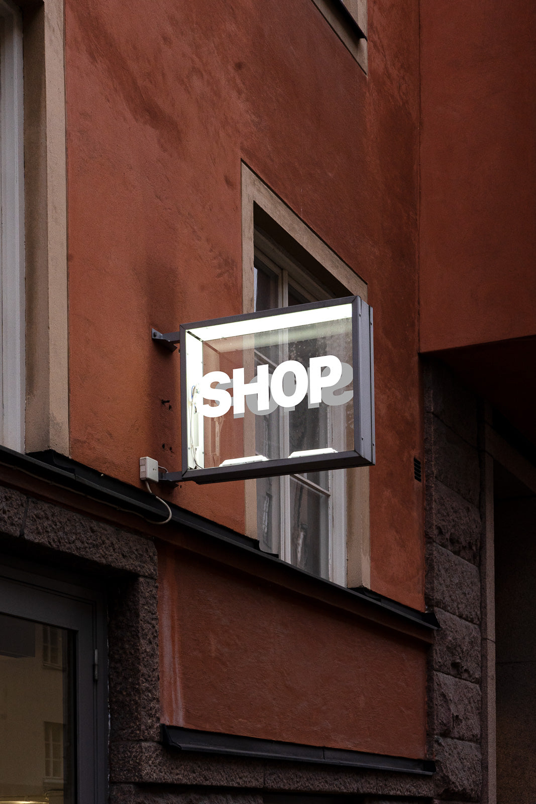 PSD mockup of a rectangular illuminated sign with the word "SHOP" on a building with a textured brick facade.