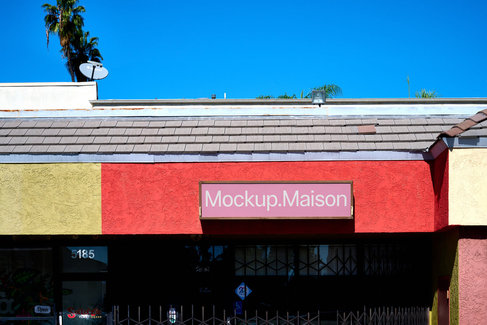 PSD mockup of a storefront with a colorful facade featuring a red, yellow, and beige design under a clear blue sky, labeled "Mockup.Maison".