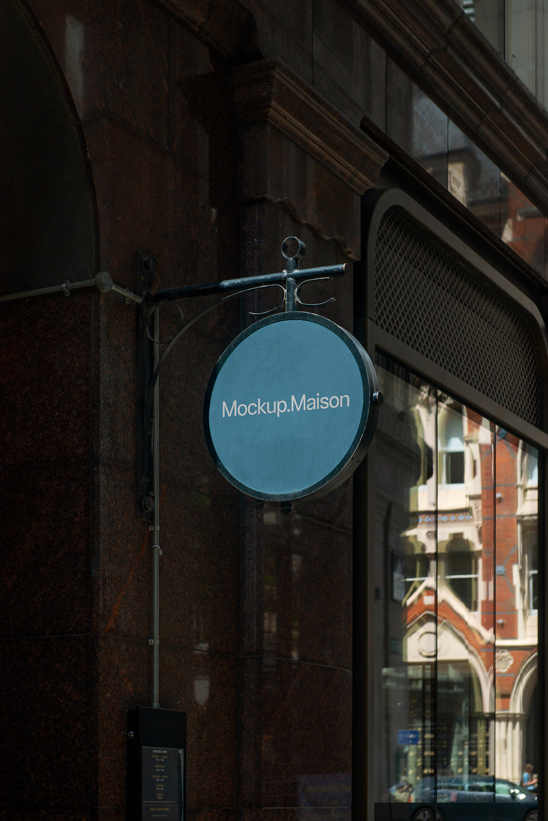 PSD mockup of a round hanging sign on a building facade with "Mockup.Maison" text, set against a reflective glass storefront showing urban architecture.