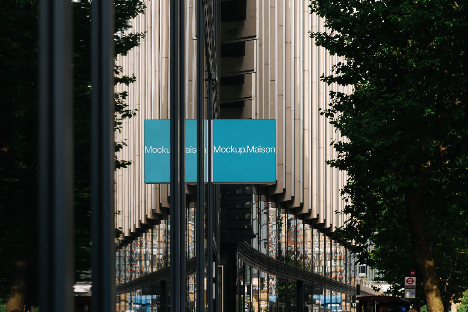 PSD mockup of a modern building facade with reflective windows and two turquoise signs reading "Mockup Maison," surrounded by trees.