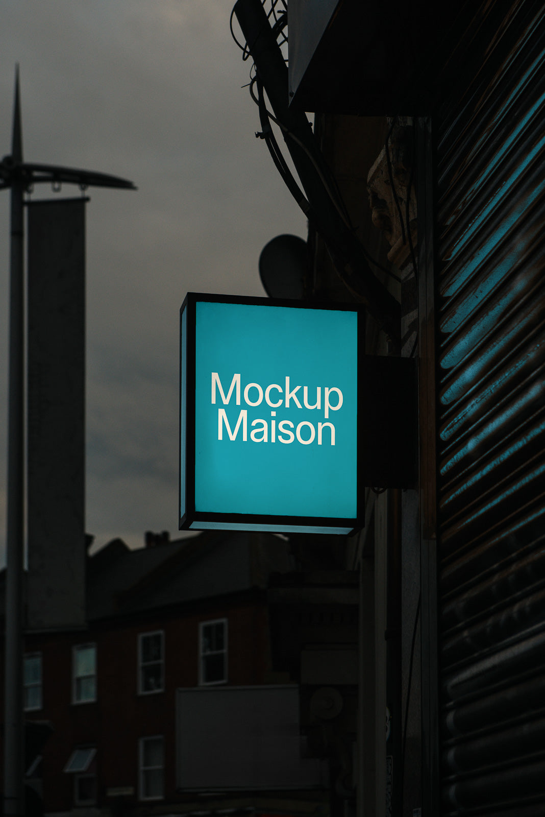PSD mockup of a square, illuminated storefront sign with "Mockup Maison" text, set against a dim urban background with buildings.