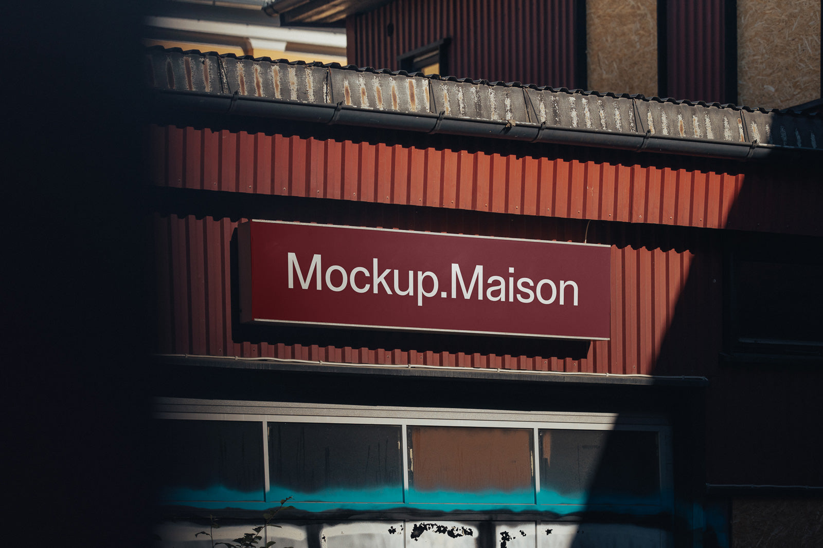 PSD mockup of a red building façade with a large rectangular sign displaying "Mockup.Maison" in white text.