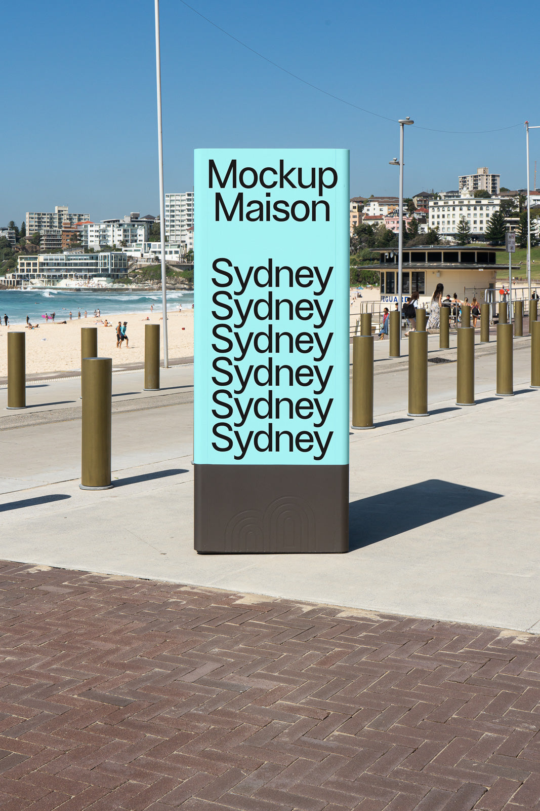 PSD mockup of a freestanding sign on a beachside promenade, displaying the text "Sydney" repeatedly. Background includes beachgoers and city buildings.