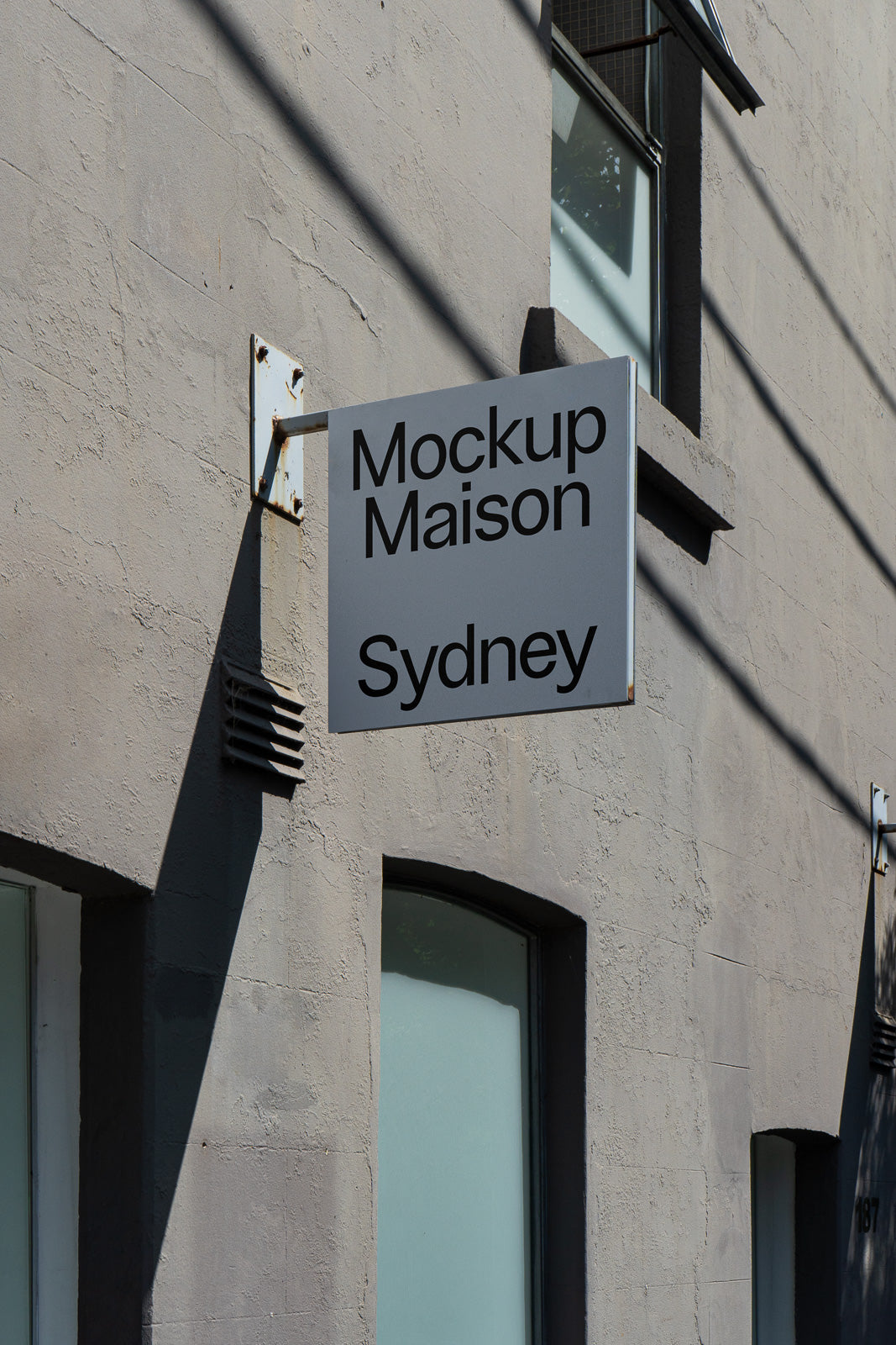 PSD mockup of a rectangular wall-mounted sign outside a building with the text "Mockup Maison Sydney" in black against a gray background.