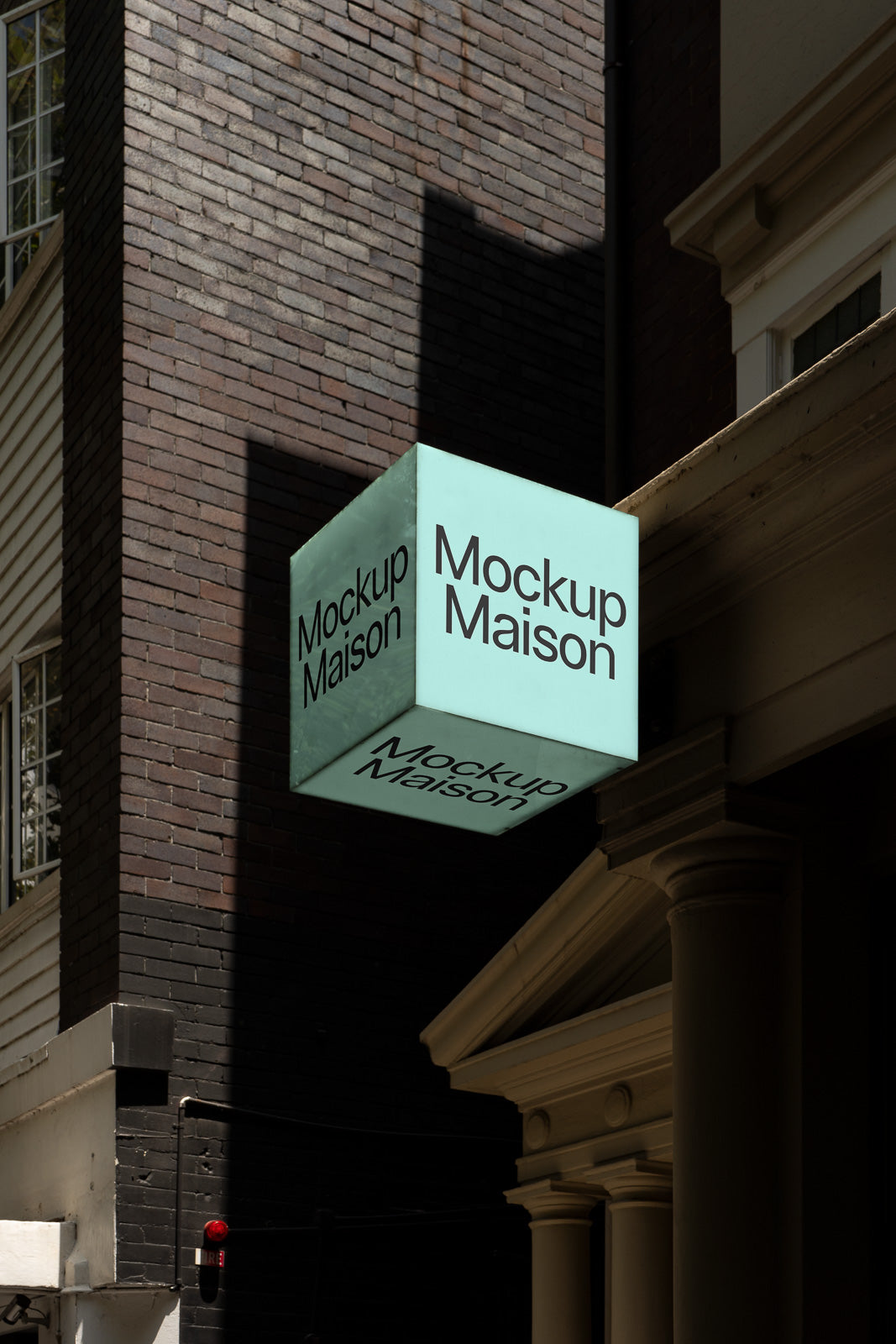 PSD mockup of a cube-shaped, teal signage affixed to a building façade, displaying the text "Mockup Maison" in a shadowy urban setting.