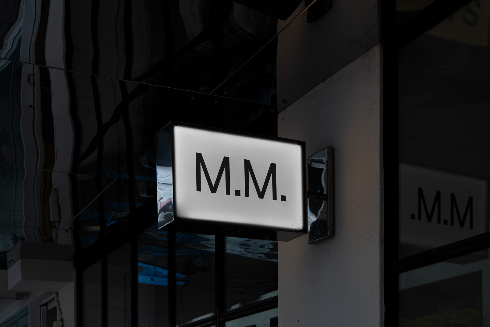 PSD mockup of an illuminated rectangular sign with the letters "M.M." displayed against a dark background, mounted on a building exterior.