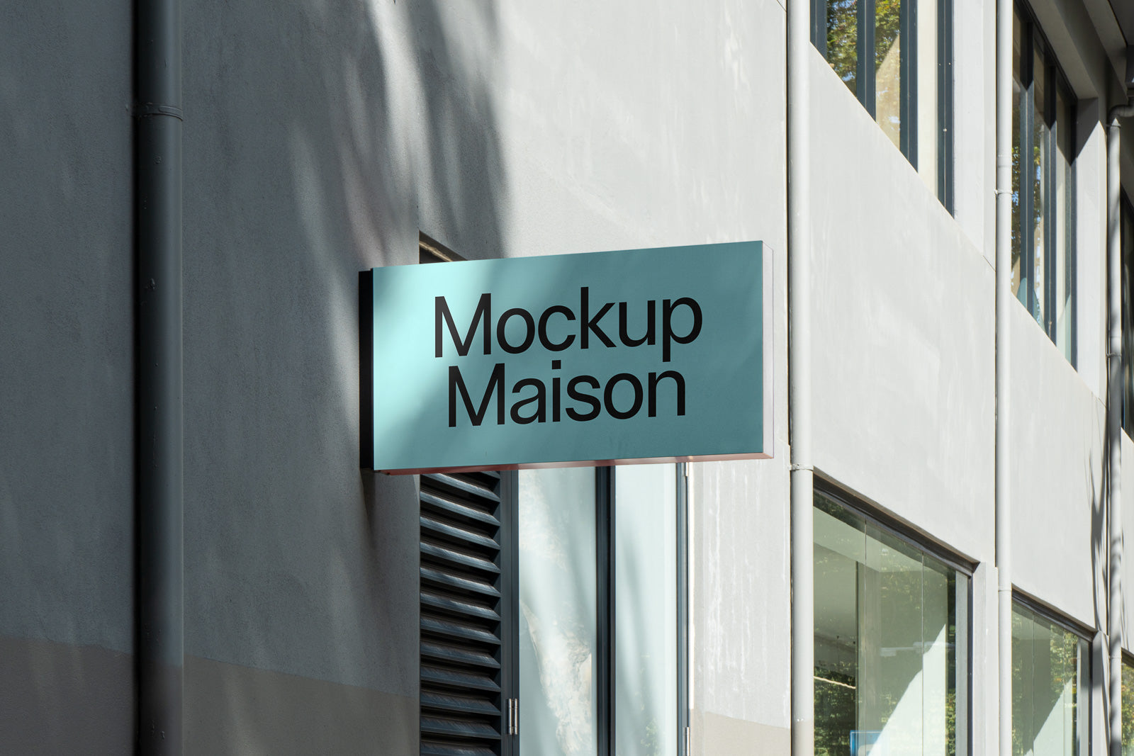 PSD mockup of a modern outdoor wall sign displaying "Mockup Maison" on a building facade with large windows and a gray exterior.