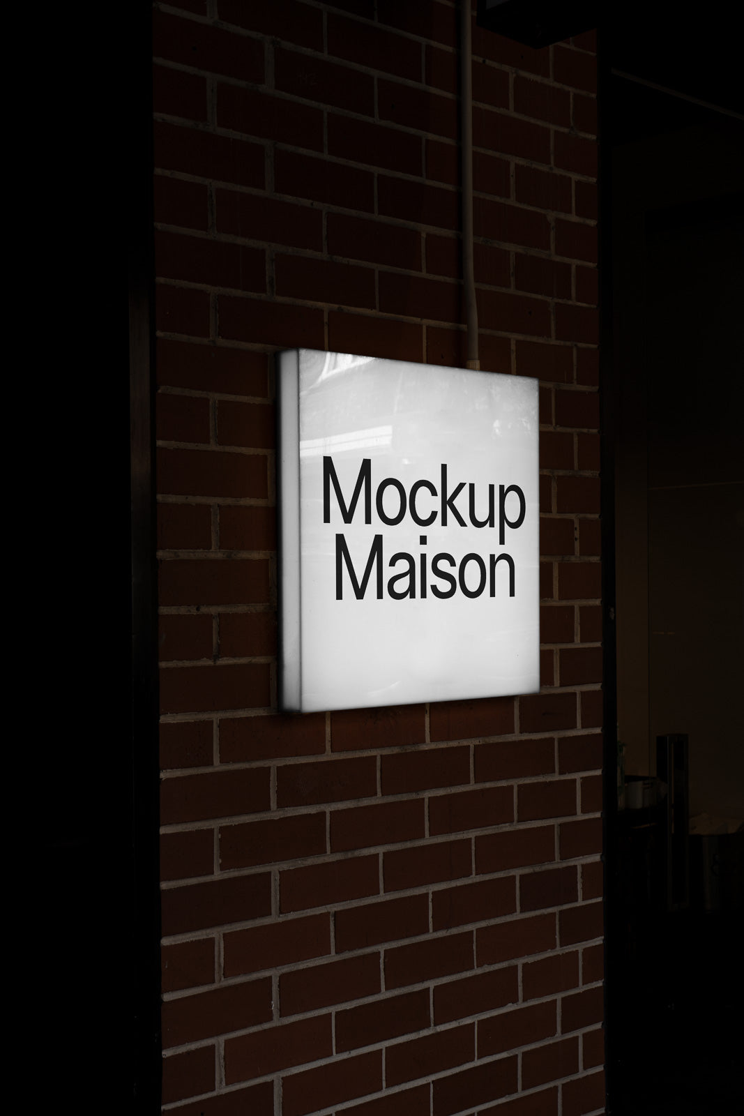 PSD mockup of an illuminated square sign displaying "Mockup Maison" mounted on a brick wall.
