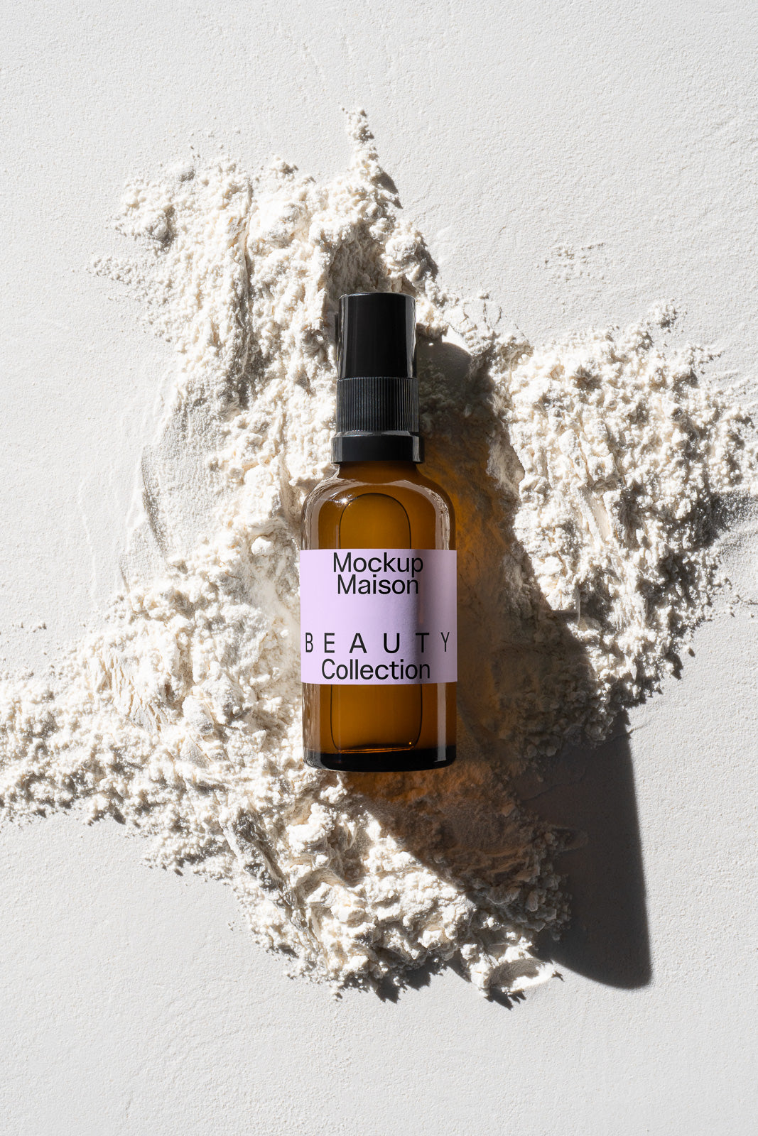 PSD mockup of an amber spray bottle labeled "Mockup Maison Beauty Collection" placed on a textured surface with scattered white powder.