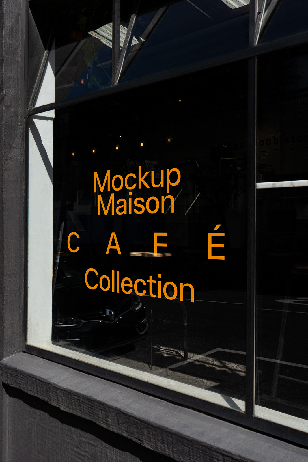 PSD mockup of a café window displaying bold orange text reading "Mockup Maison CAFE Collection" with reflections and interior visible.