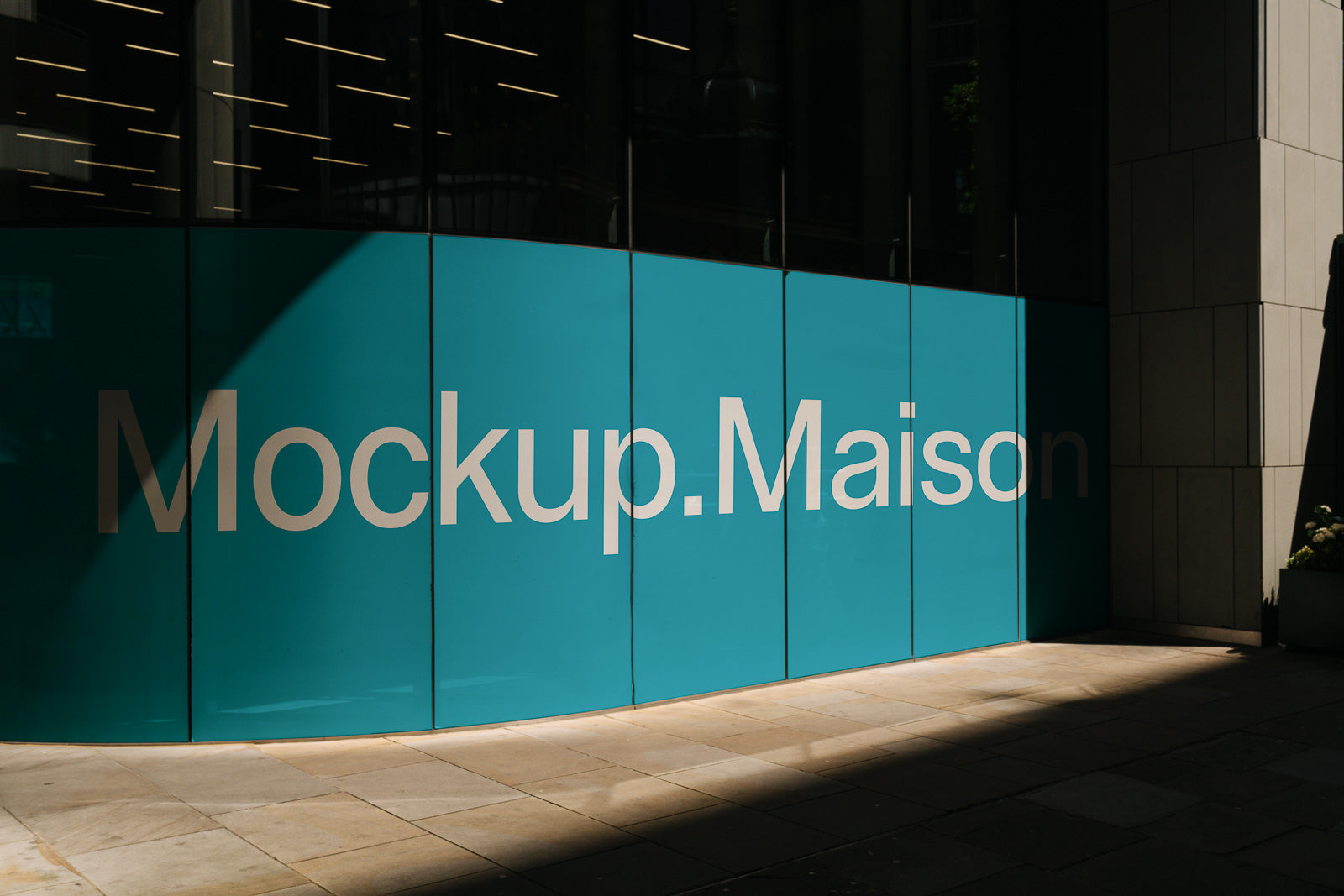 PSD mockup of a large storefront window with the text "Mockup.Maison" in bold white letters on a bright teal background.