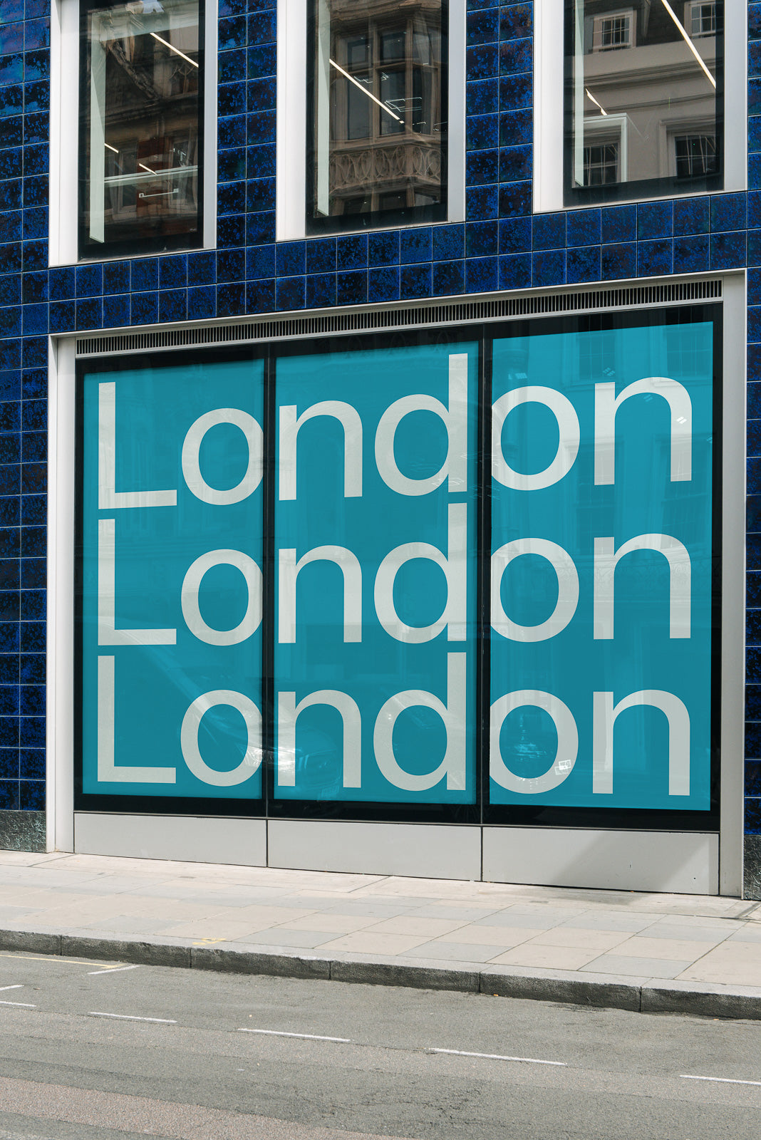 PSD mockup of a storefront window display with large, repeated white "London" text on a teal background, reflecting urban architecture.