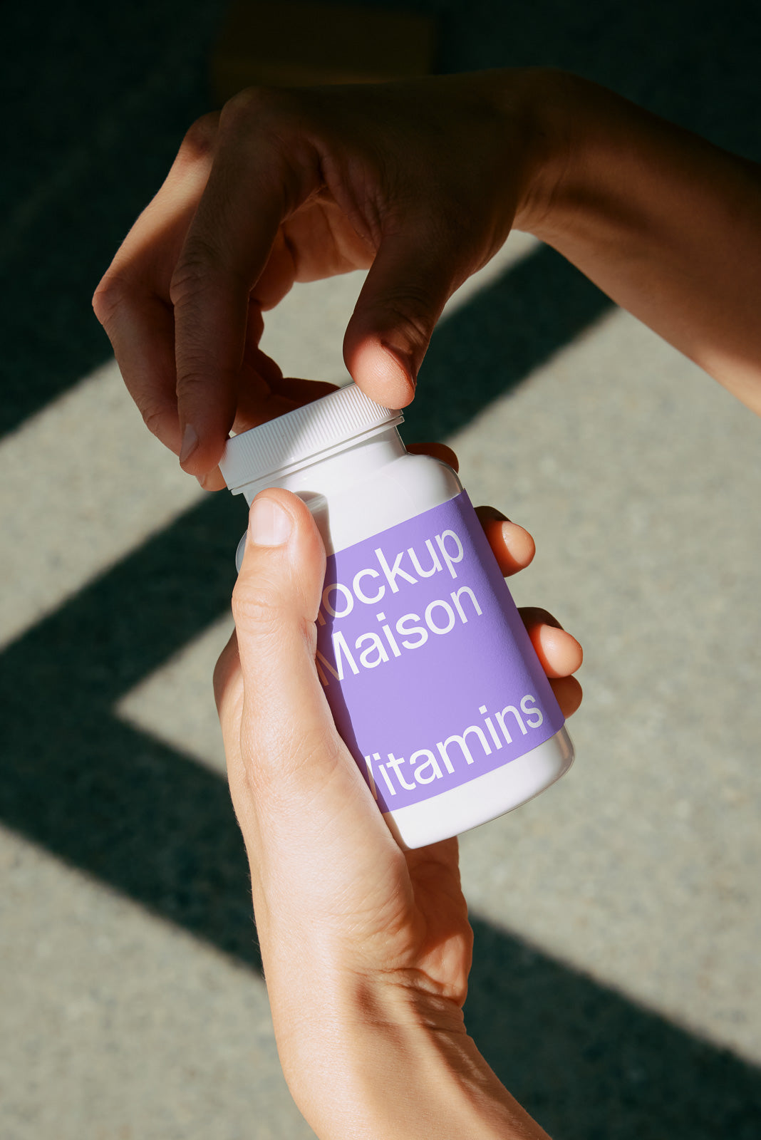 PSD mockup of a hand opening a vitamin bottle with a purple label in natural lighting.