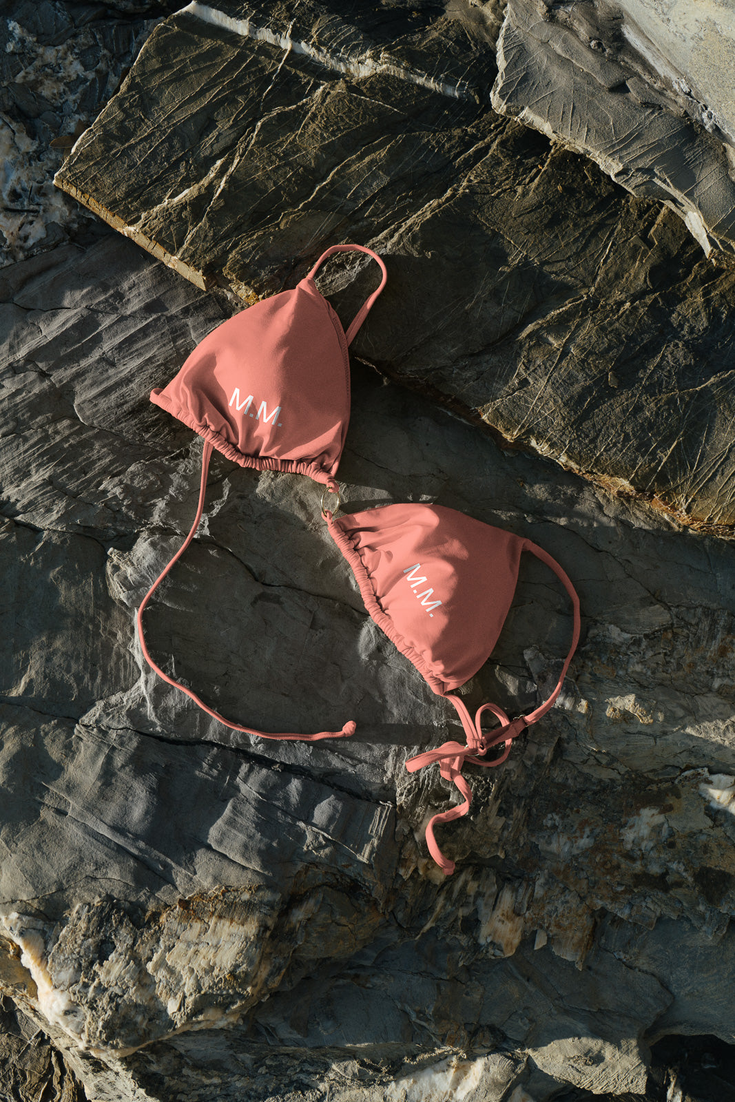 PSD mockup of a coral bikini top with "N.M." initials on rocky surface, capturing natural light and texture contrast.