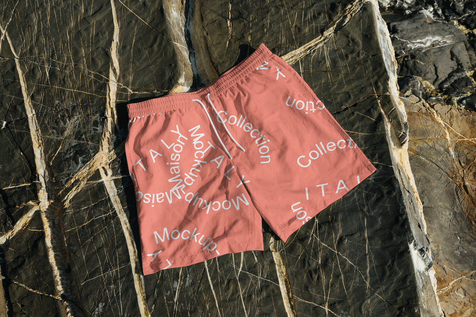PSD mockup of pink shorts with white text, including "Mockup" and "Collection", placed on a textured stone surface with intricate patterns.