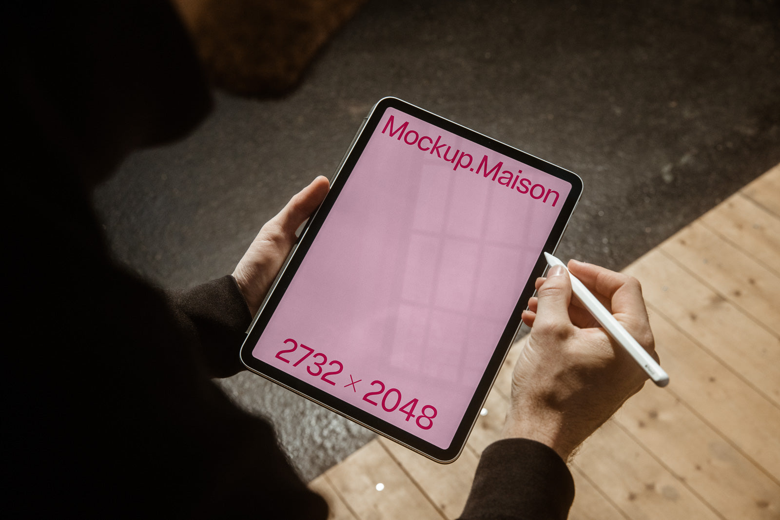 PSD mockup of a tablet displaying a pink screen with "Mockup.Maison" text and dimensions "2732 x 2048," being used with a stylus in a warm-lit room.