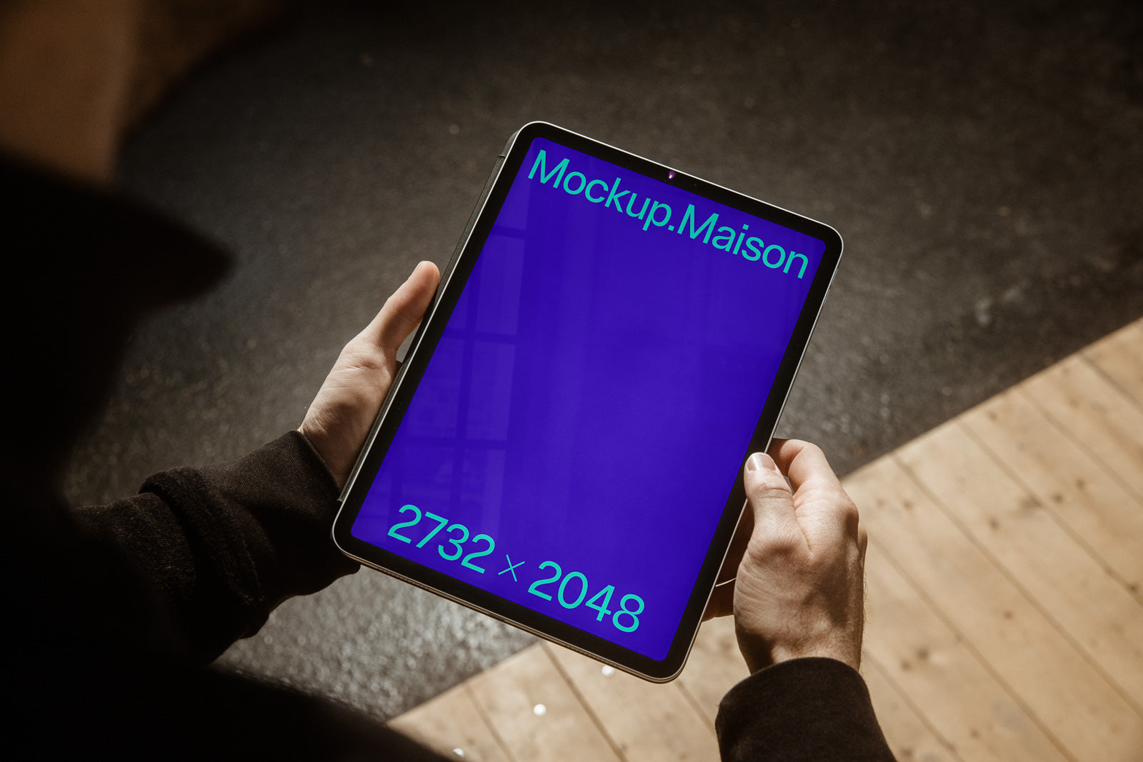 PSD mockup of a person holding a tablet displaying a blue screen with the text "Mockup.Maison" and "2732 x 2048" in a natural light setting.