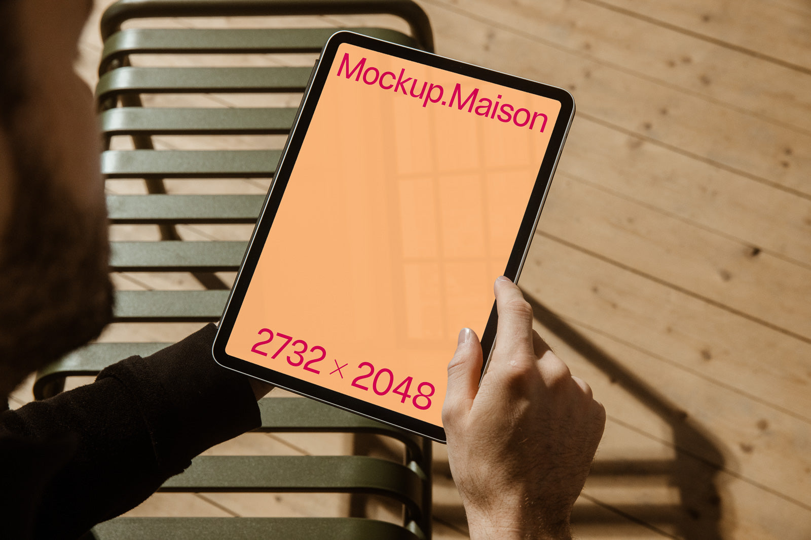 PSD mockup of a tablet held by a person in one hand, displaying a blank orange screen with text "Mockup.Maison" and "2732 x 2048" in a wooden floor setting.
