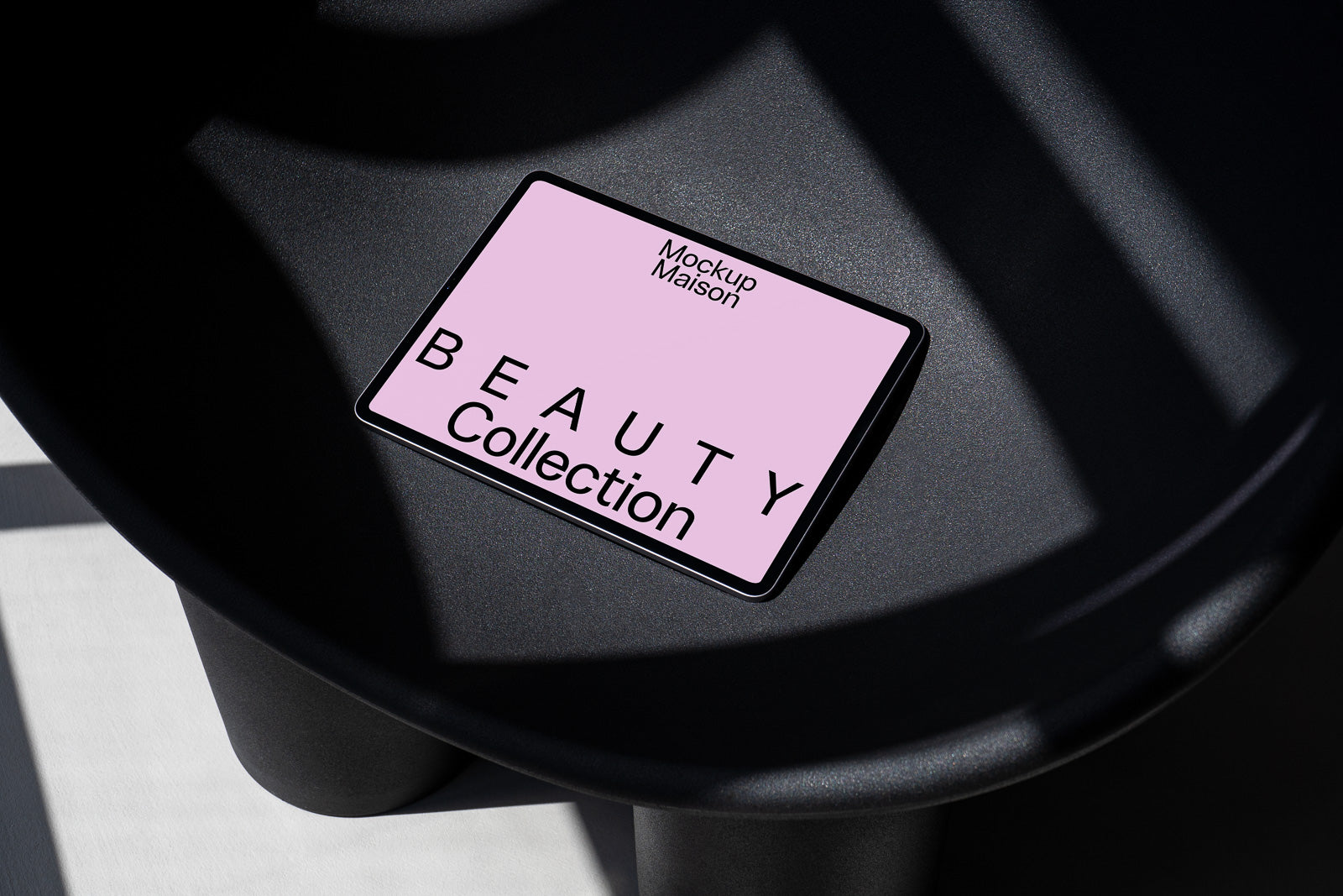 PSD mockup of a tablet showcasing "Beauty Collection" text with "Mockup Maison" on a pink background, placed on a dark textured surface with shadows.