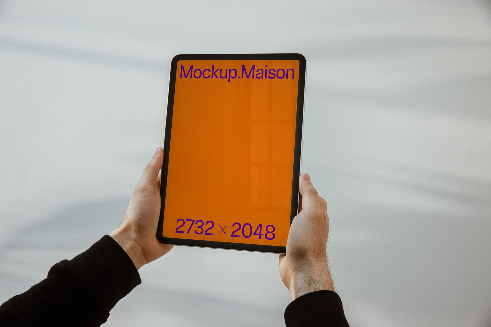 PSD mockup of a tablet held by hands, displaying an orange screen with the text "Mockup.Maison" at the top and "2732 x 2048" at the bottom.