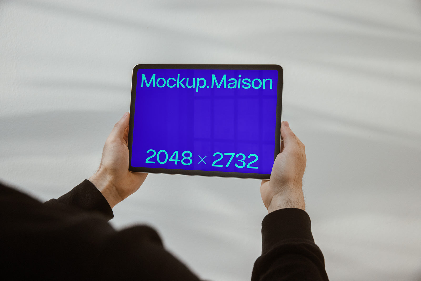 PSD mockup of a person holding a tablet with a blue screen displaying the text "Mockup.Maison" and dimensions "2048 x 2732" in green.