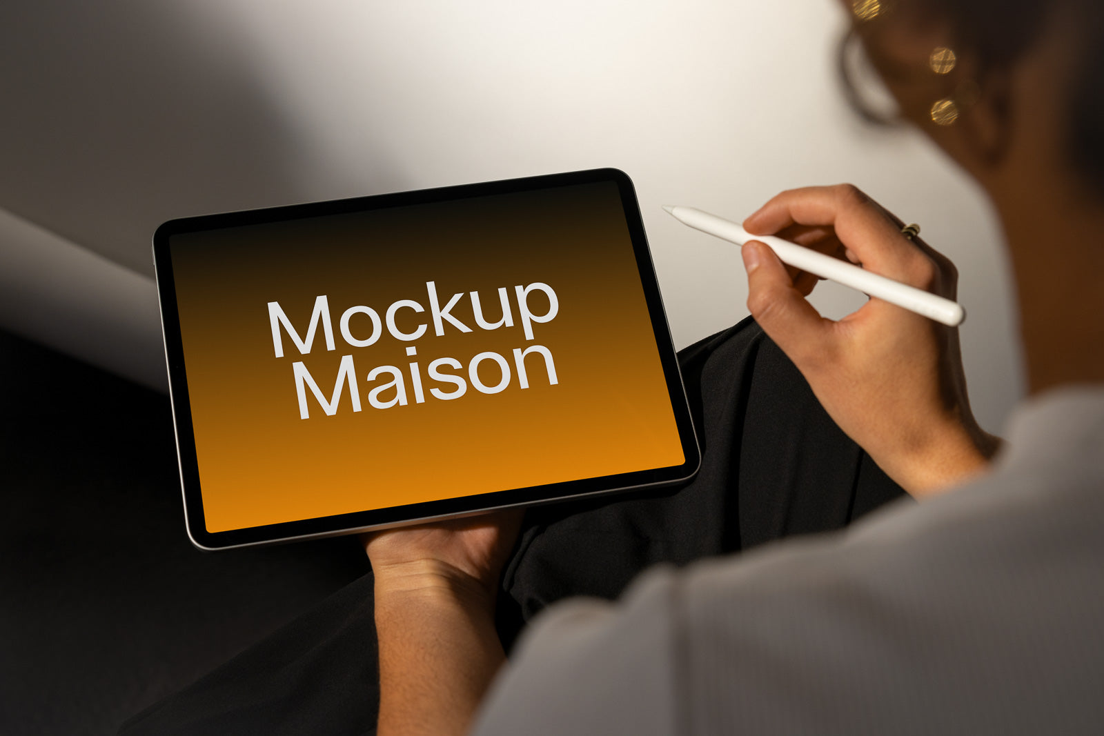 PSD mockup of a tablet displaying the text "Mockup Maison" on an orange gradient screen, held by a person using a stylus pen.