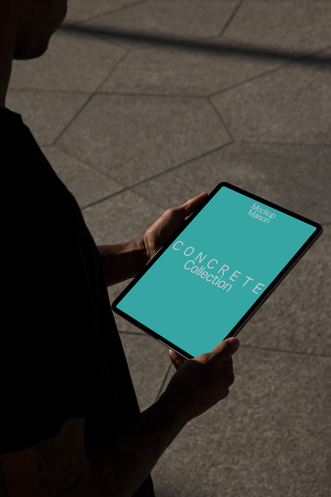 PSD mockup of a person holding a tablet displaying a green screen with the text "Concrete Collection" on an outdoor stone tile surface.