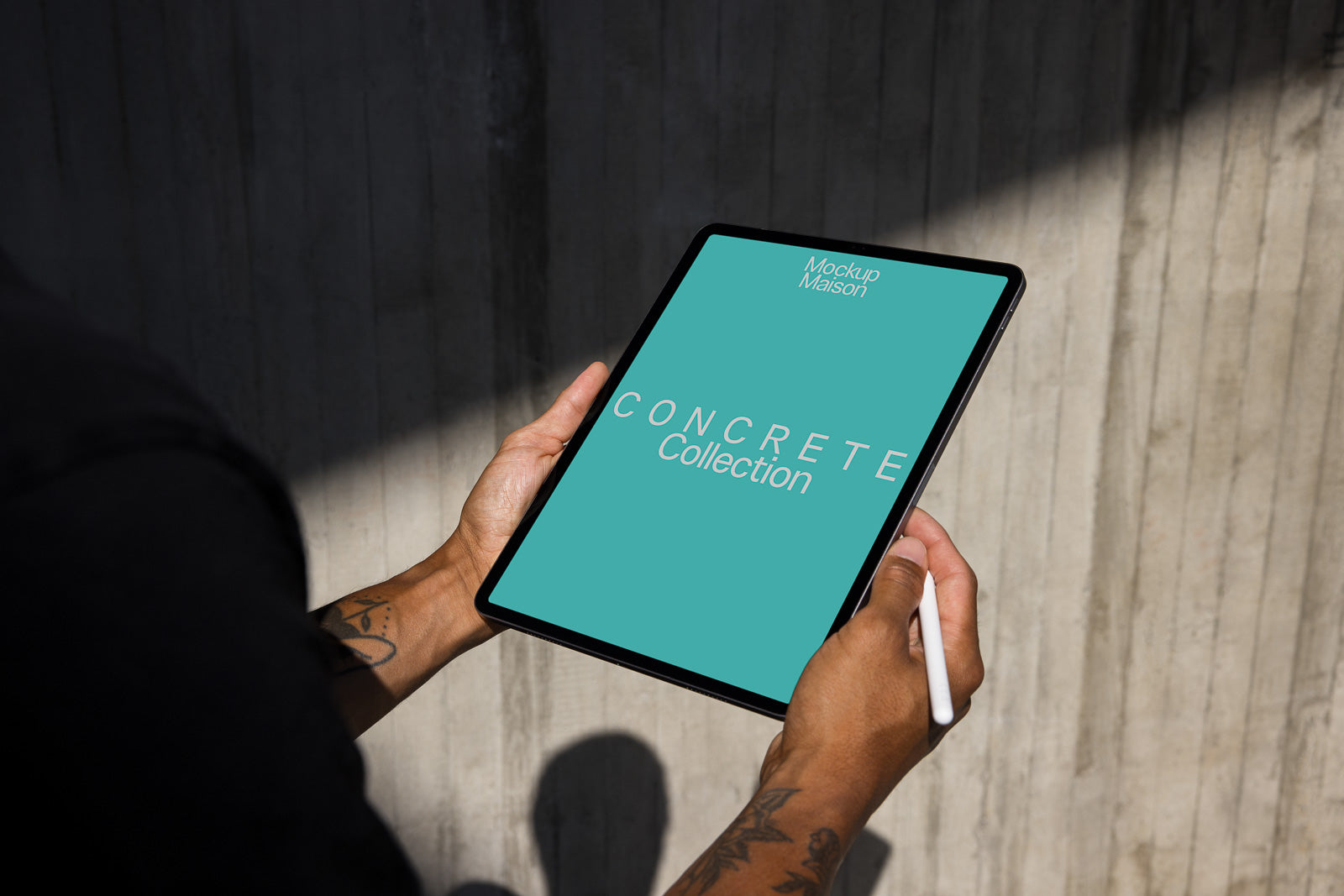 PSD mockup of a person holding a tablet displaying "Concrete Collection" on a turquoise screen, with a stylus in hand, casting shadows on a textured surface.