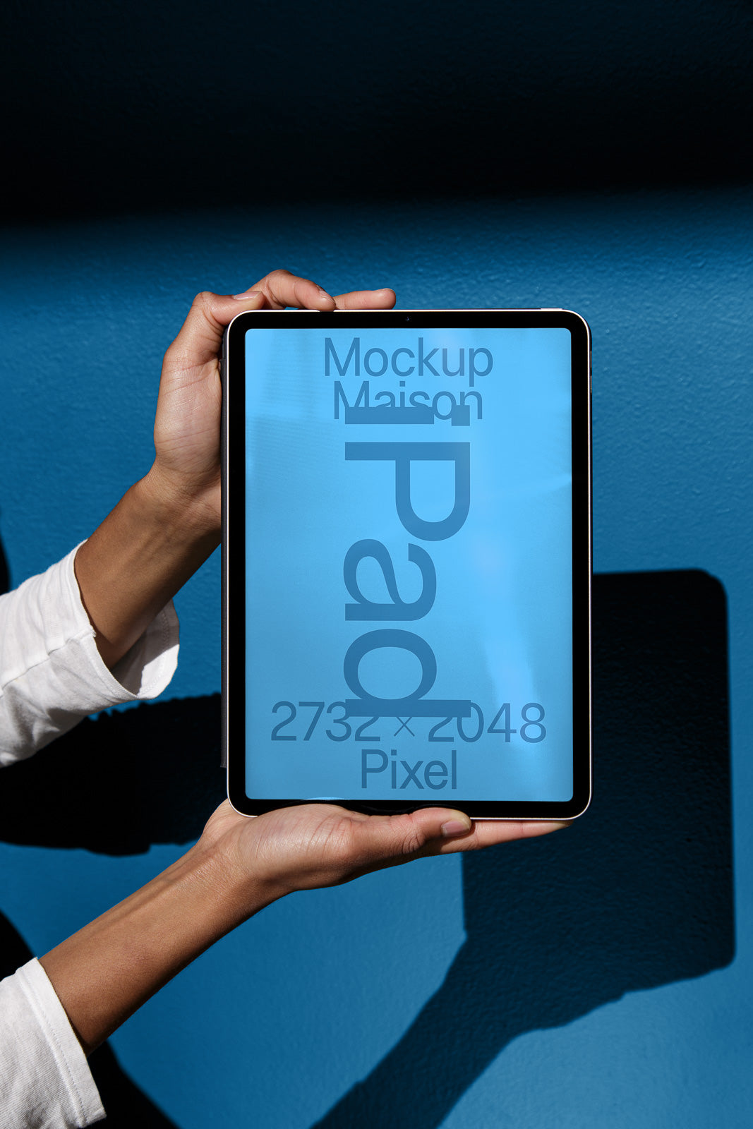 PSD mockup of a tablet held in hands against a blue background, displaying text and dimensions on the screen.
