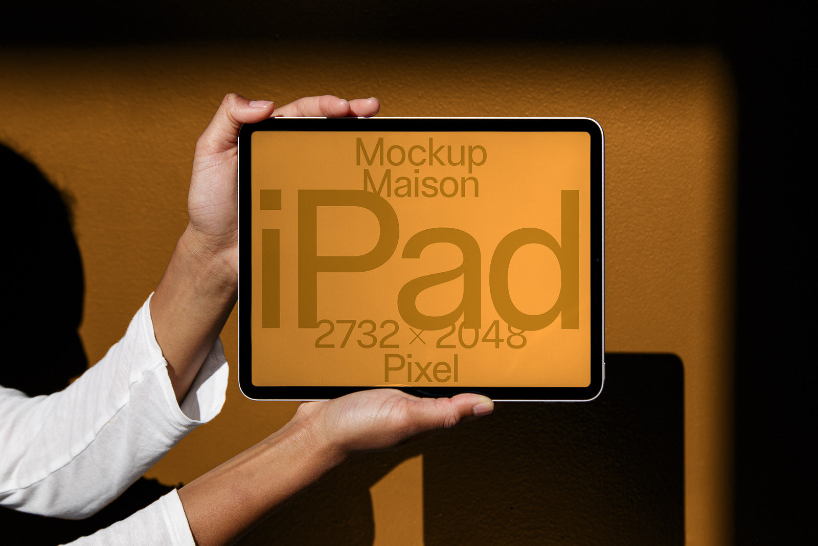 PSD mockup of a tablet held by hands against a warm, textured background, displaying text details such as "iPad" and "2732 x 2048 Pixel" on its screen.
