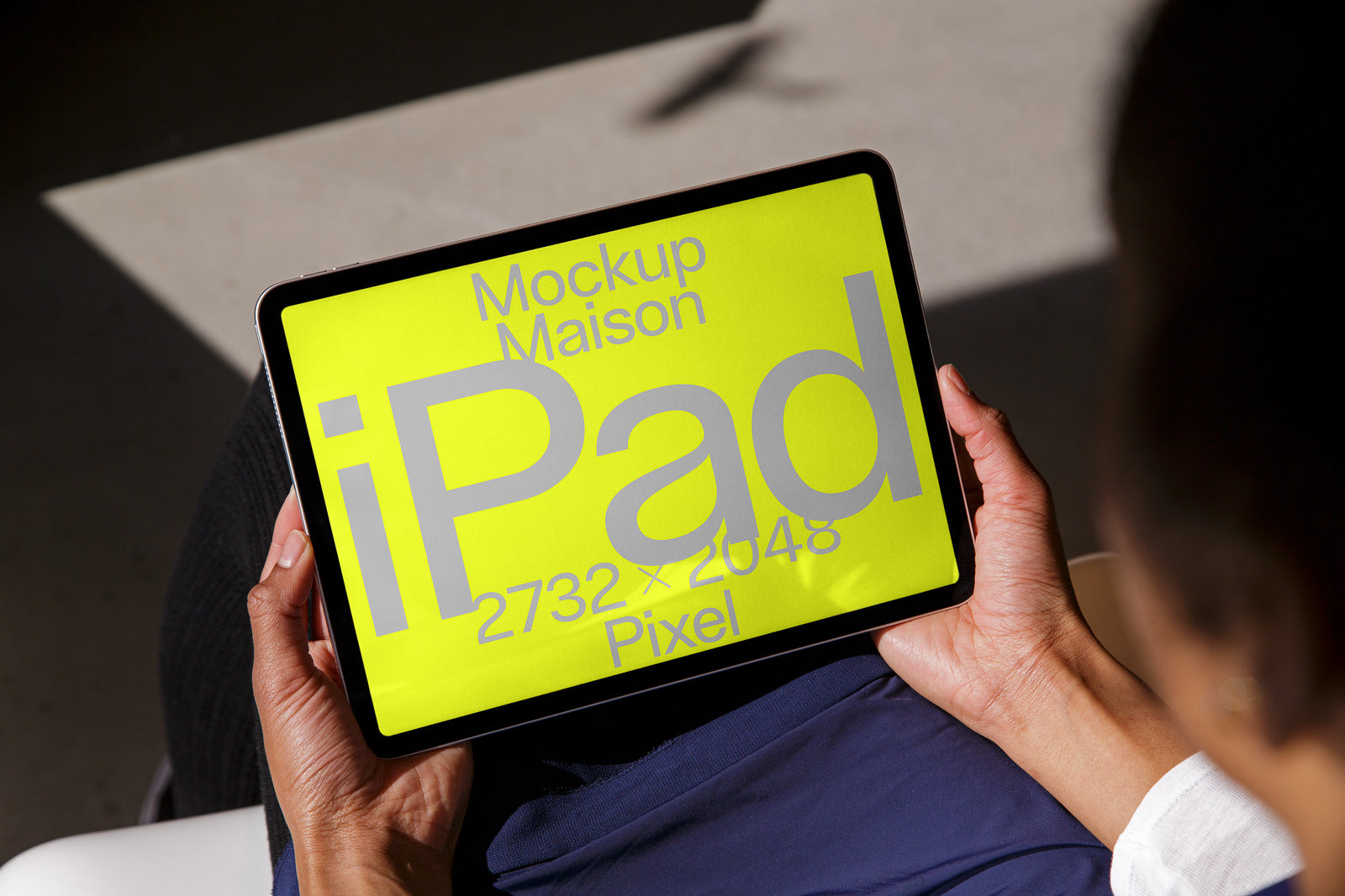 PSD mockup of a person holding an iPad displaying "Mockup Maison iPad 2732 x 2048 Pixel" on a bright yellow screen, set against a casual indoor background.